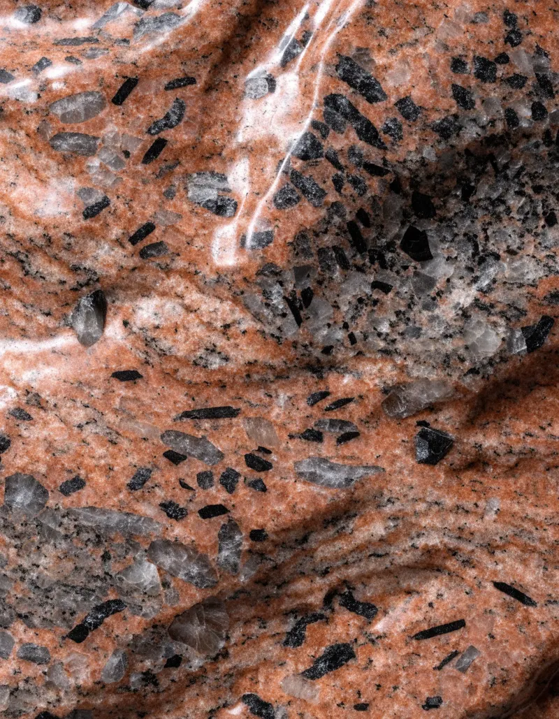 A polished slab of Red Aswan granite, brick-red feldspar flecked with grey quartz and dark mica